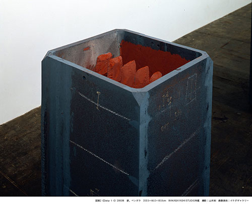 青黒い鉄の箱の中に赤い鉄が何本も収まっている作品