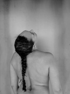長い髪を1本に結った後ろ姿の裸の女性上半身のモノクロ写真