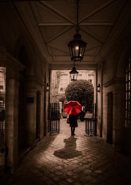 赤い傘を指す人が歩くパリの路地